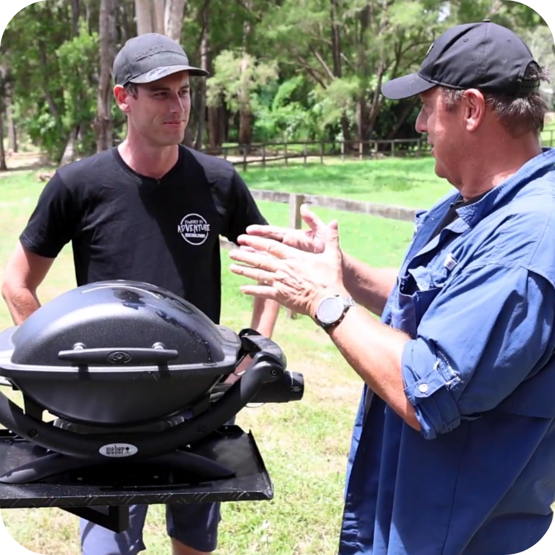 Channel 7's Creek to Coast Scotty Hillier of Creek to Coast and Charlie from Everything Caravan & Camping demonstrate the Weber BabyQ on a BBQARM swing-arm table. 